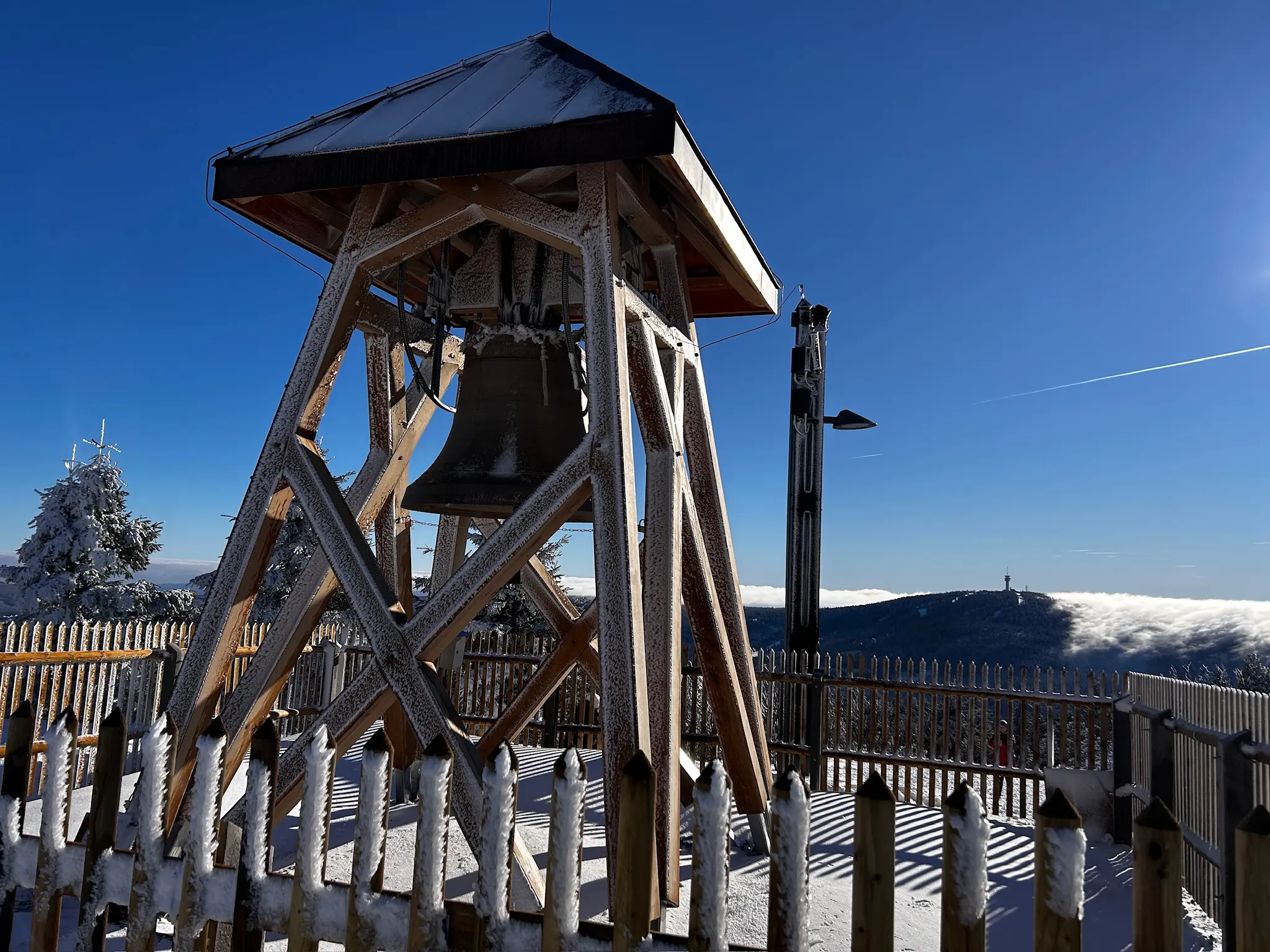 The iced Peace Bell and wooden frame against the blue sky, with the cloud-covered ridge beyond