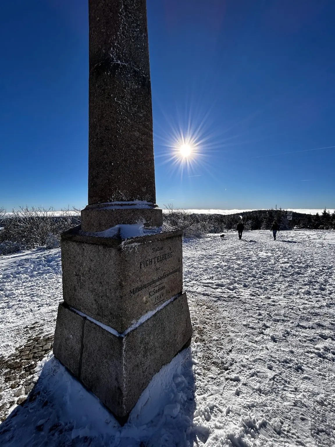 The Fichtelberg surveying column standing in snow beneath a bright winter sun