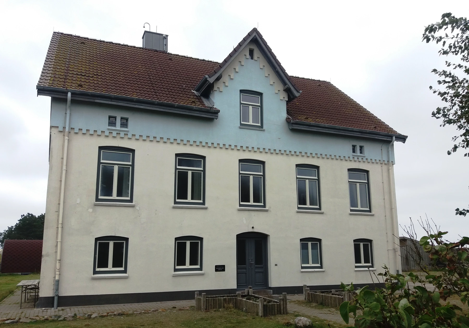 Front of the pale pilots’ house, with rows of windows, a central gable and a tiled roof.